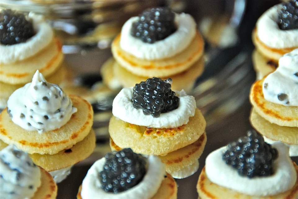 Close-up van een blini met crème fraîche en kaviaar op een spiegelend dienblad.